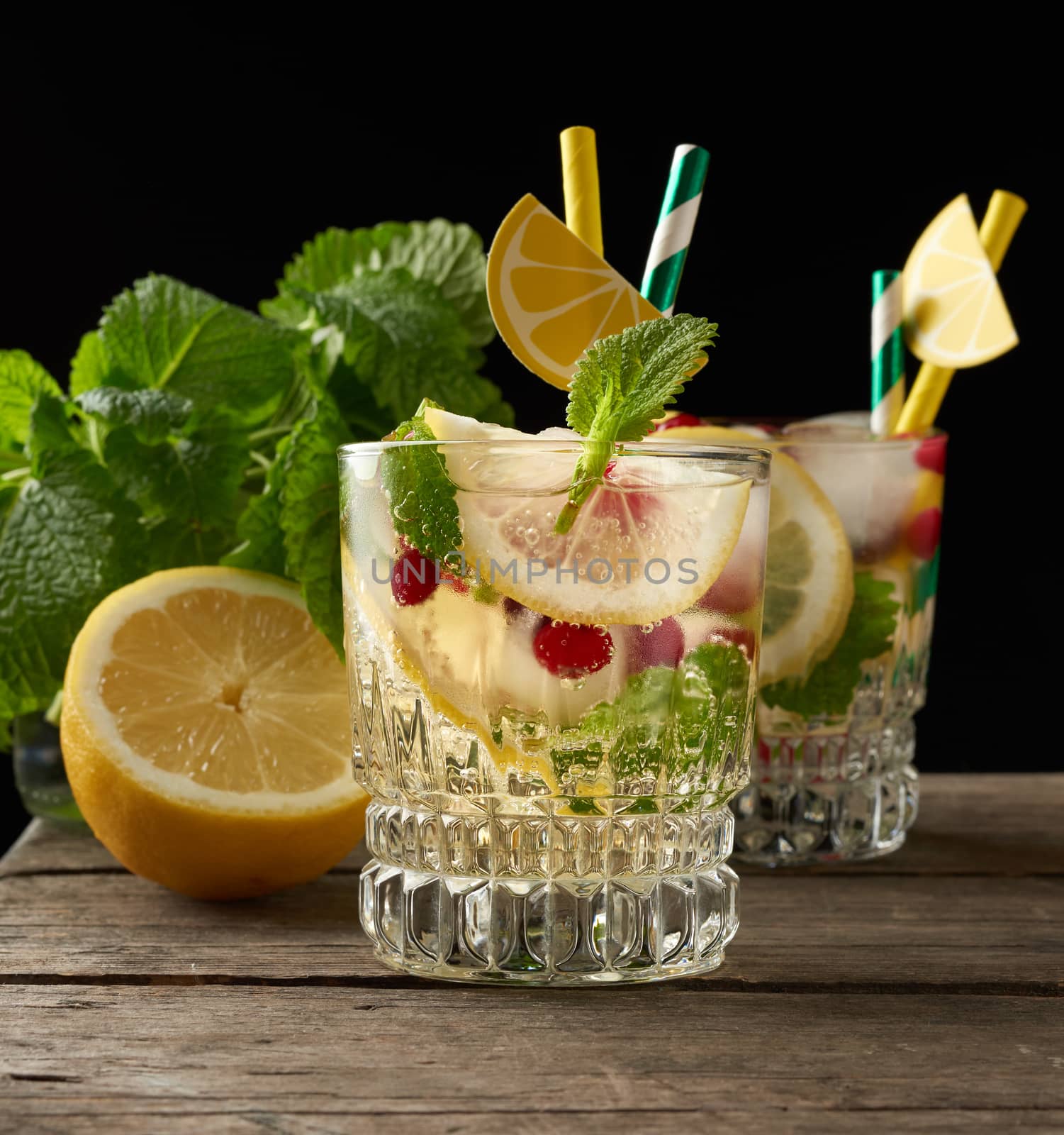 transparent glass with lemonade and pieces of ice, red berries, a refreshing summer drink on a black background 