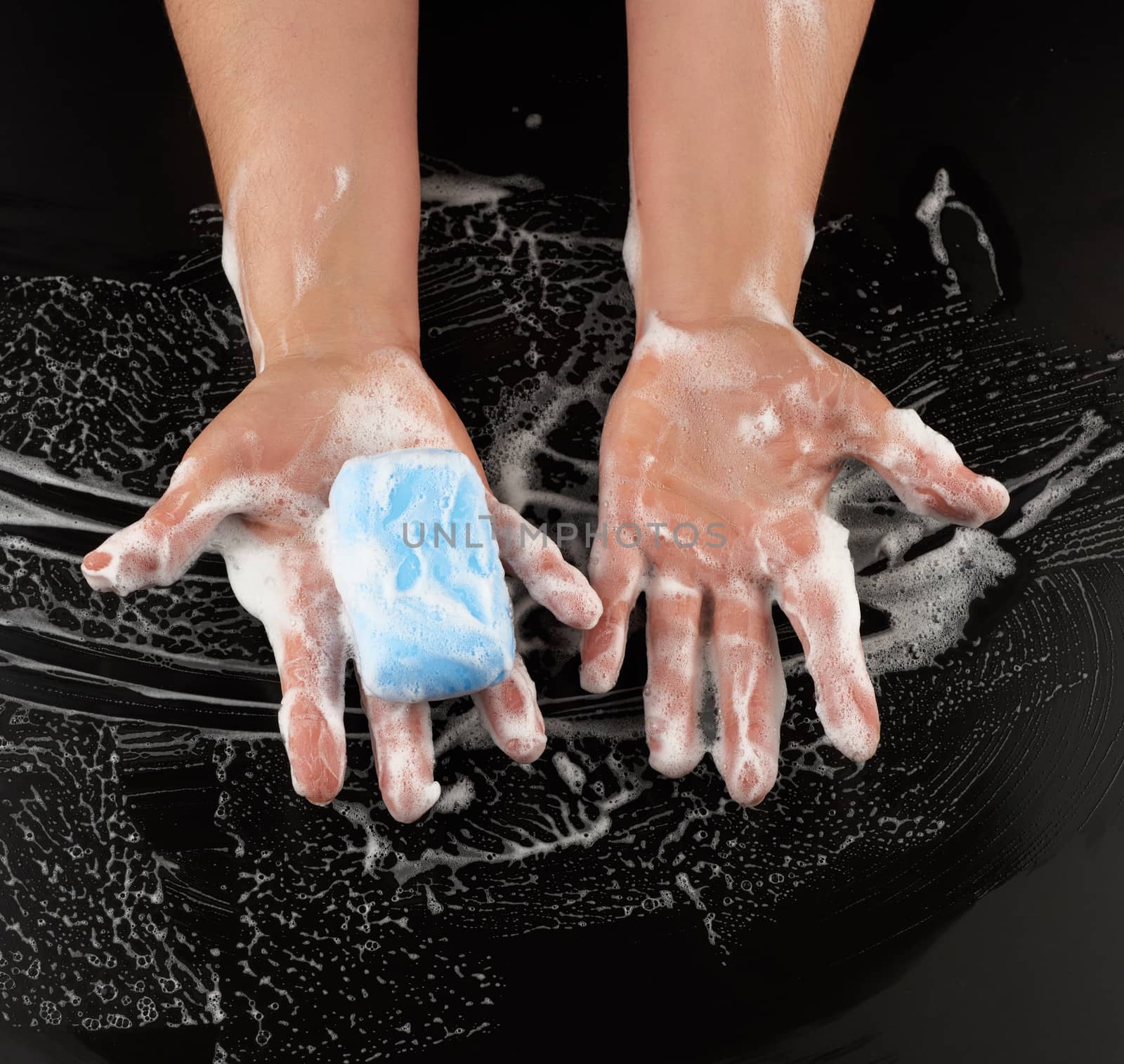 process of washing hands with blue soap, parts of the body in white foam on a black background, top view, hygiene concept