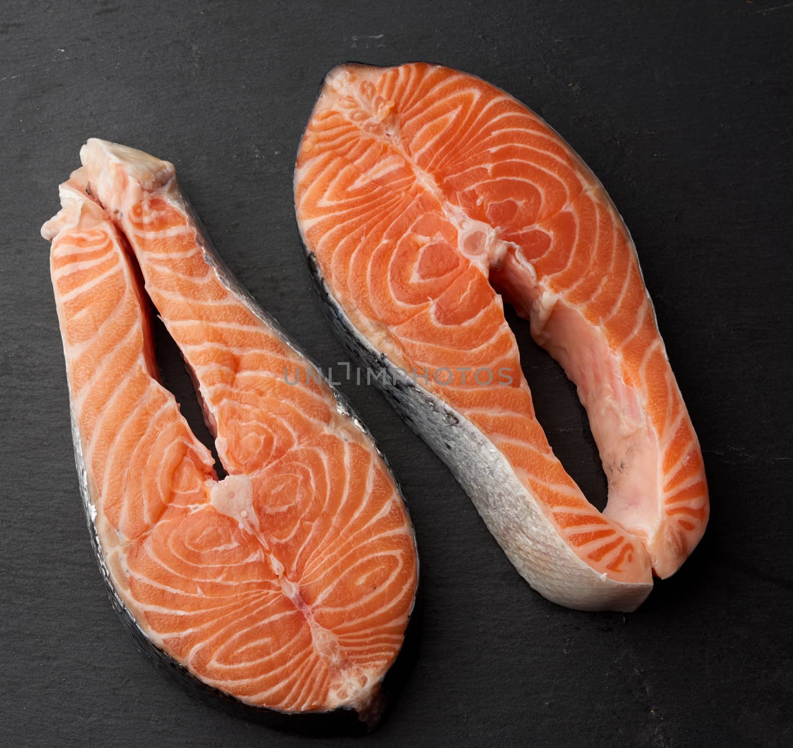 two raw salmon steaks on a black background, top view