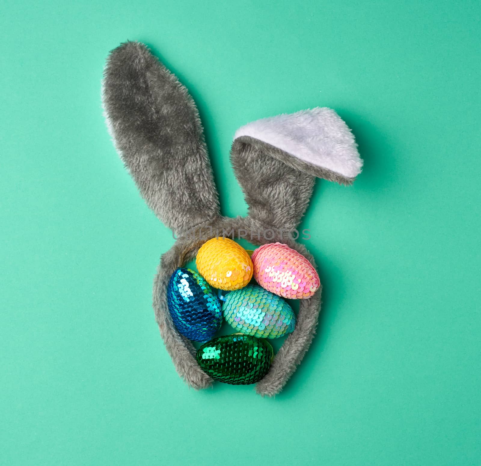 multicolored decorative Easter eggs decorated with sequins and rabbit mask on the head with ears on a green background, festive backdrop, top view