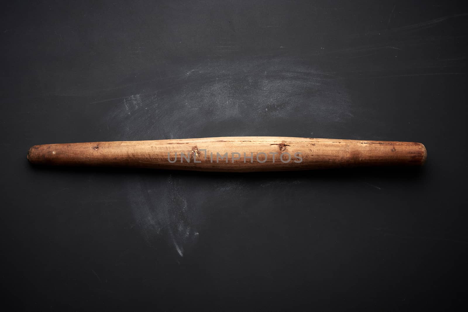 very old wooden rolling pin for rolling dough on a black background, top view