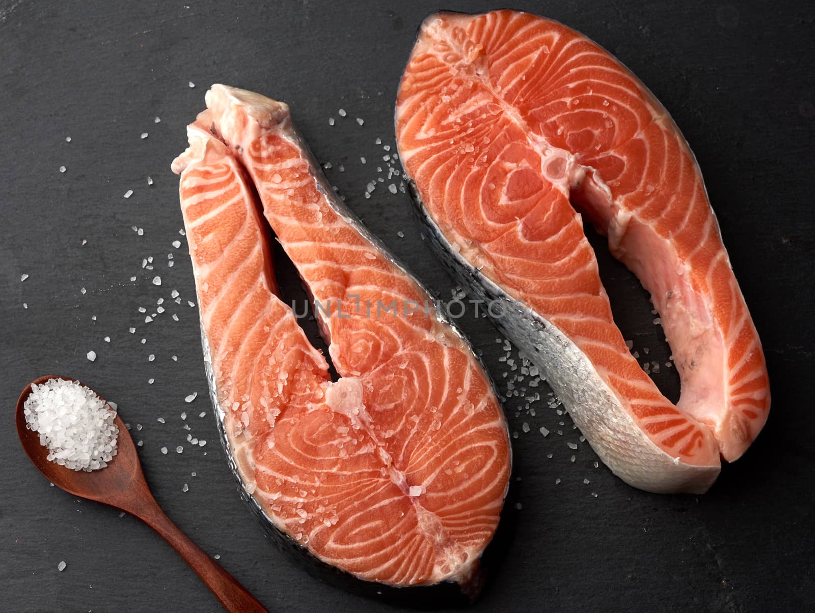 two raw salmon steaks with white salt on a black background, top view