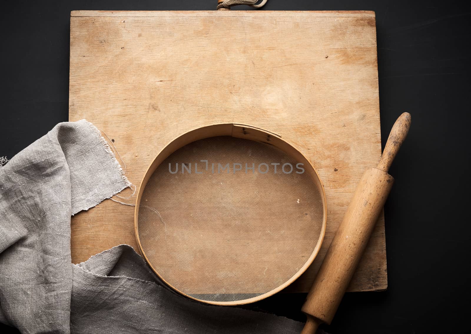 vintage wooden rolling pin and a round sieve, gray linen napkin, black table, top view, cooking utensils for making dough