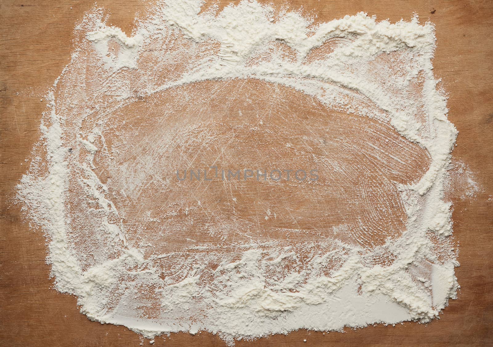 white wheat flour scattered on a brown wooden table, top view, kitchen backdrop, copy space
