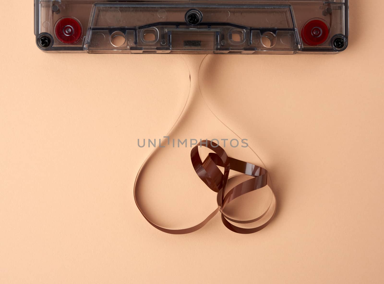 cassette with a brown magnetic tape on a beige background, the tape is tangled, top view