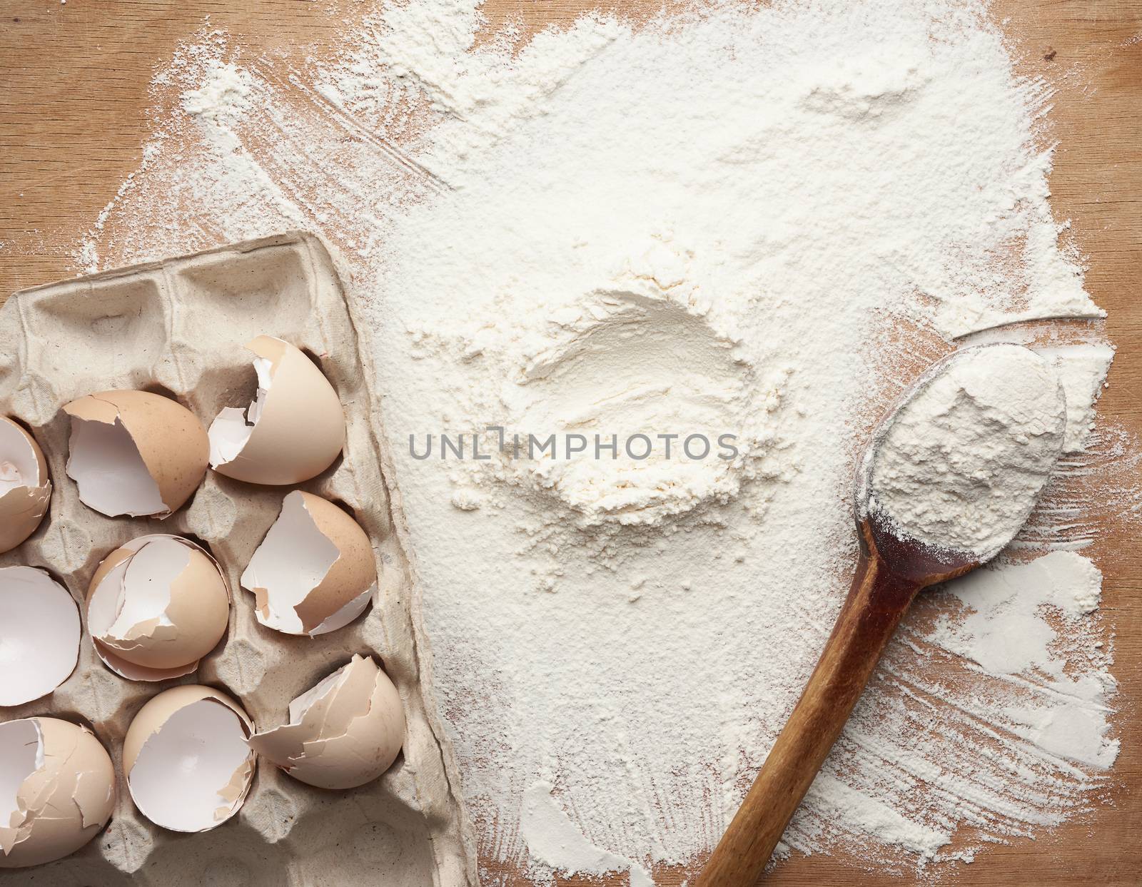 white wheat flour scattered on a brown wooden table, top view, funnel for liquid ingredients