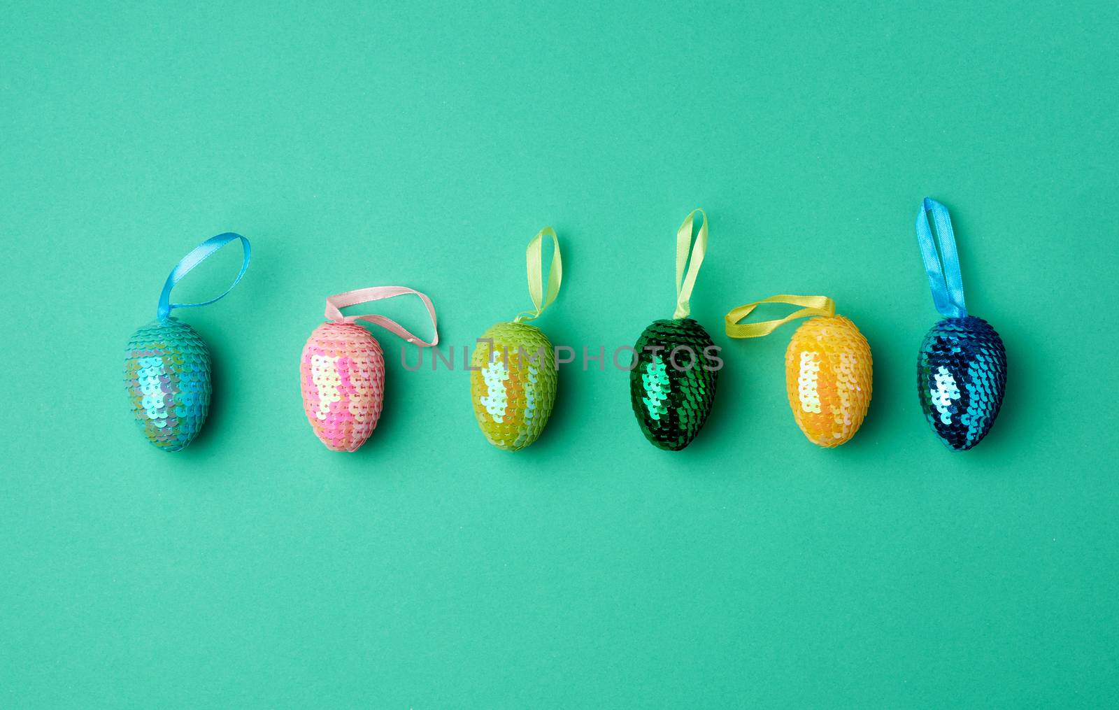 multicolored decorative Easter eggs decorated with sequins on a green background, festive backdrop, top view