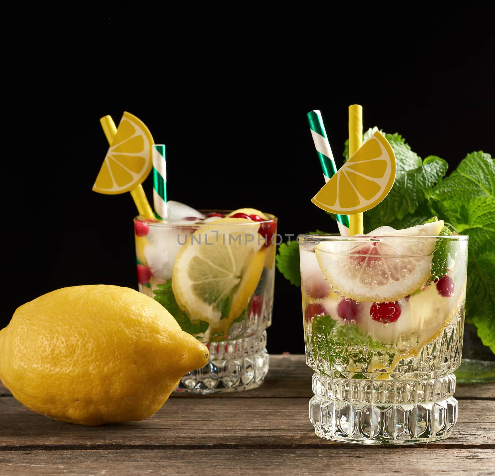 transparent glass with lemonade and pieces of ice, red berries, a refreshing summer drink on a black background 