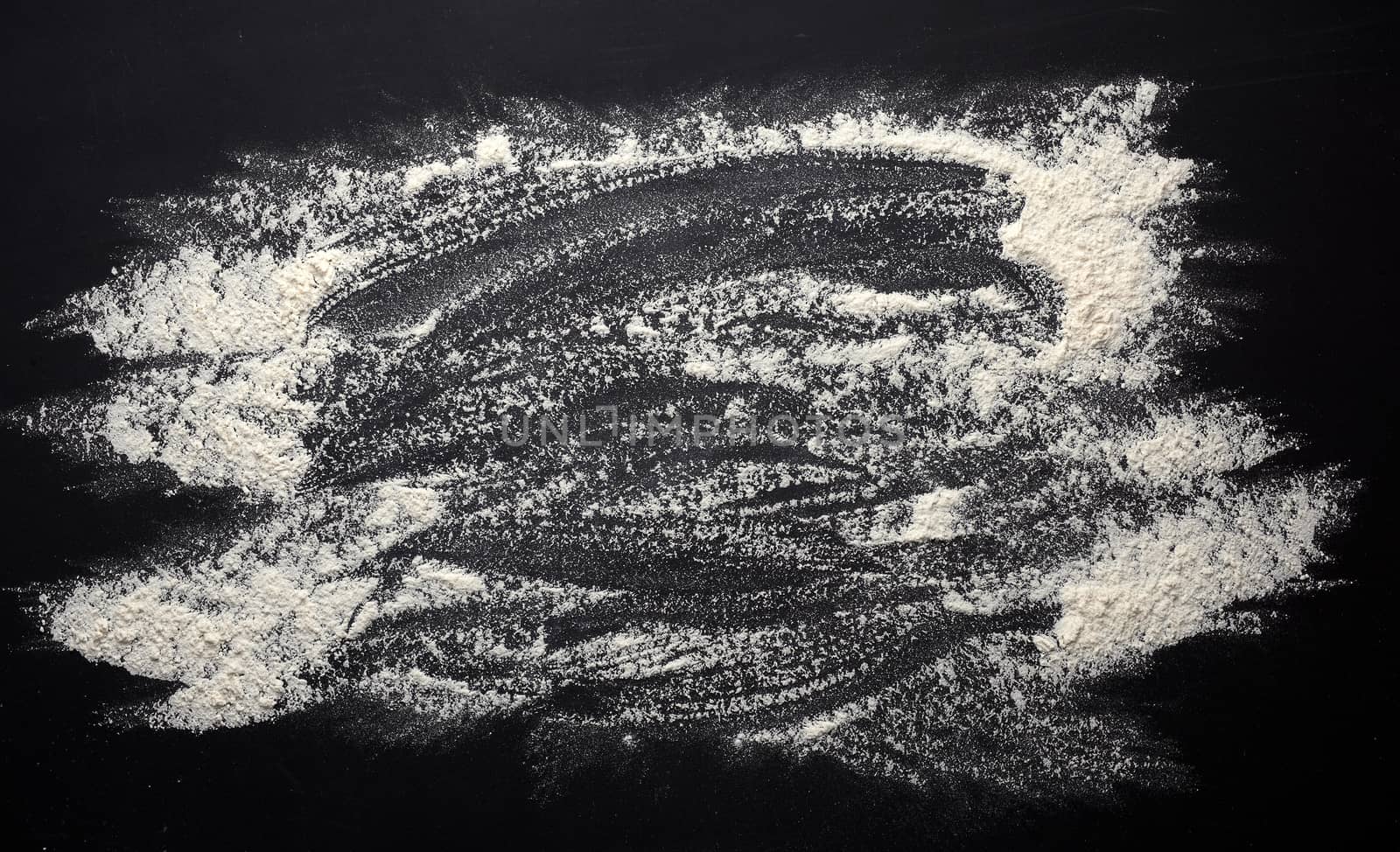 white wheat flour scattered on a black wooden table, top view, kitchen backdrop, copy space