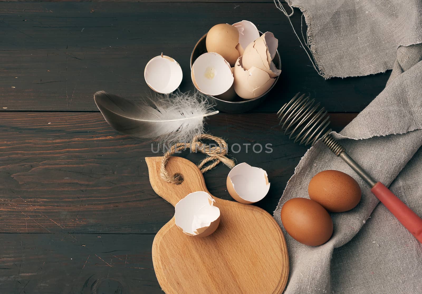 brown raw chicken eggs, shells, cutting board and hand-held whisk for protein on a wooden table, top view