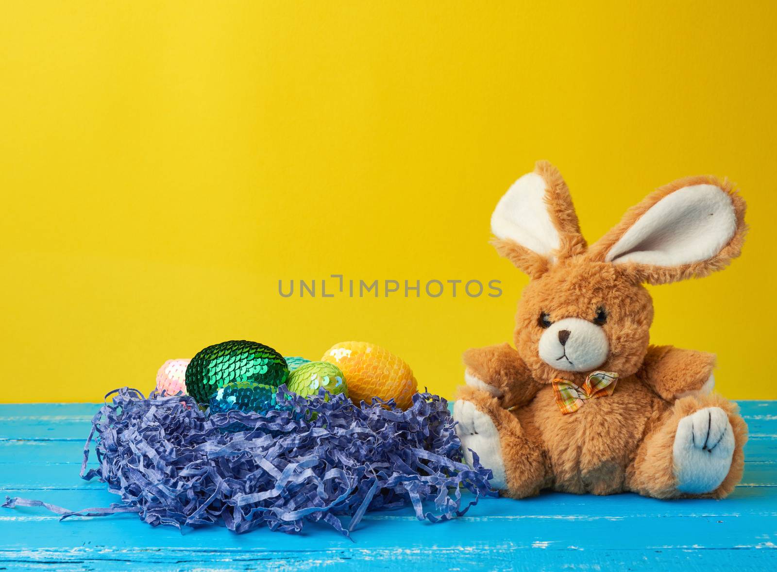 cute rabbit toy and decorative Easter eggs with sequins on a yellow background, festive backdrop