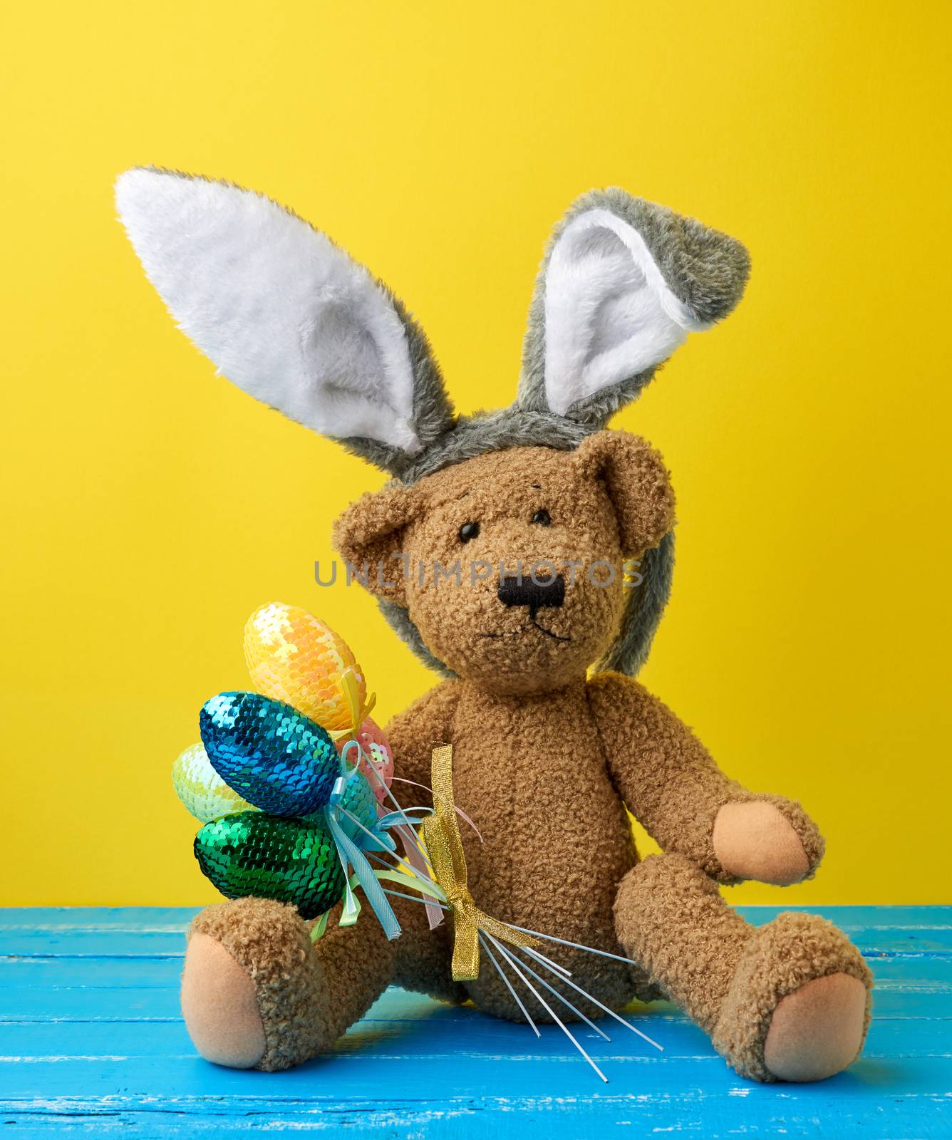 vintage cute brown teddy bear holding colorful Easter eggs, wearing a rabbit mask with long ears on his head, funny holiday card
