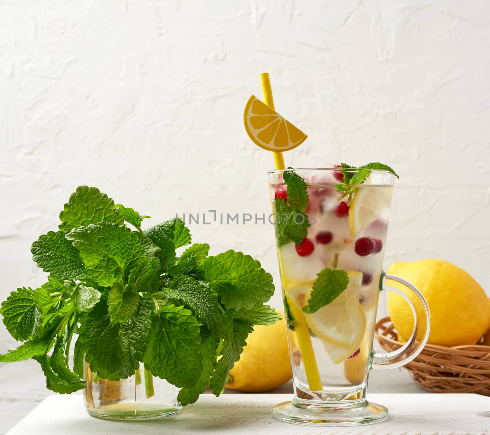transparent glass with lemonade and pieces of ice, red berries and paper tubes, a refreshing summer drink