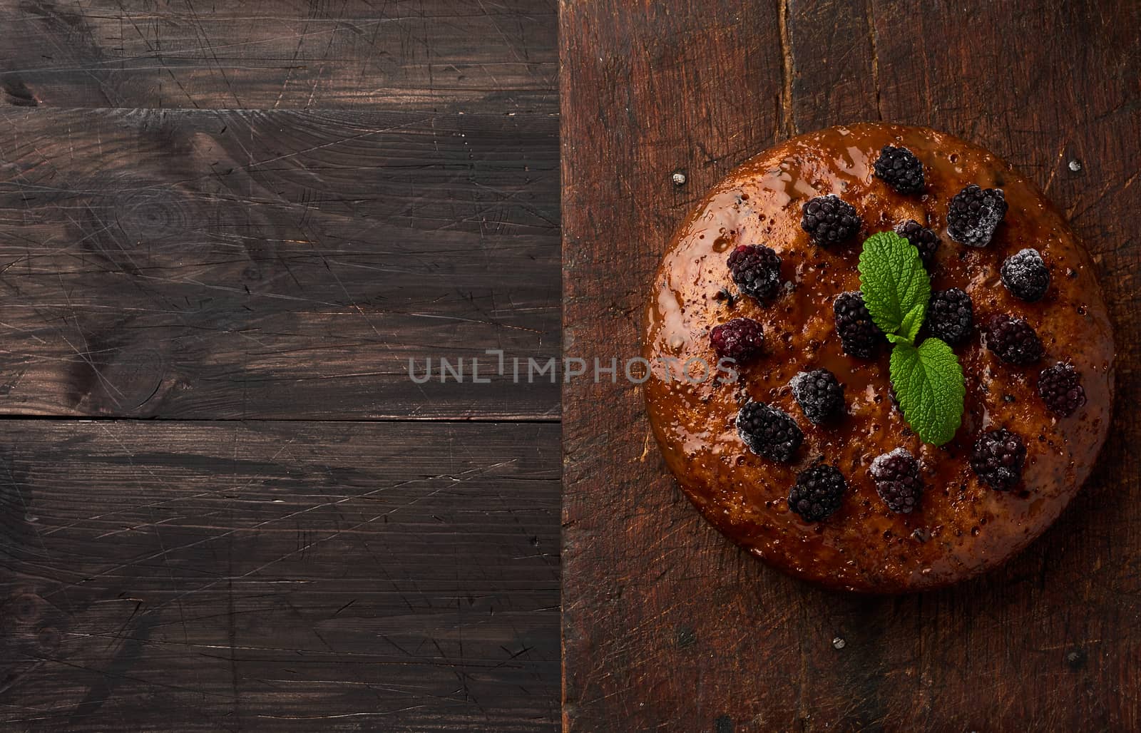 baked round biscuit cake with nuts and berries topped, wooden brown table, top view, copy space 