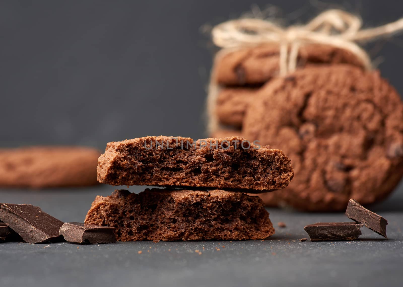 stack of baked round chocolate chip cookies and pieces of chocolate on a black table, close up