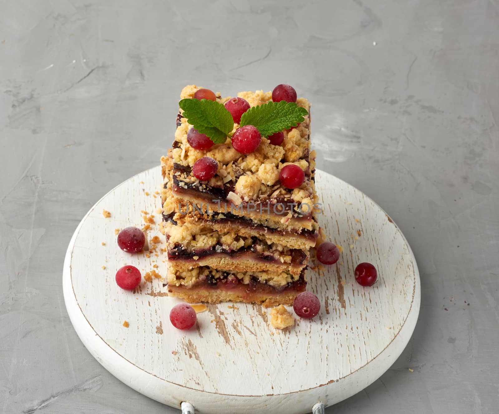 stack of square slices of baked crumble pie with blue plum on a white wooden board, delicious dessert, top view