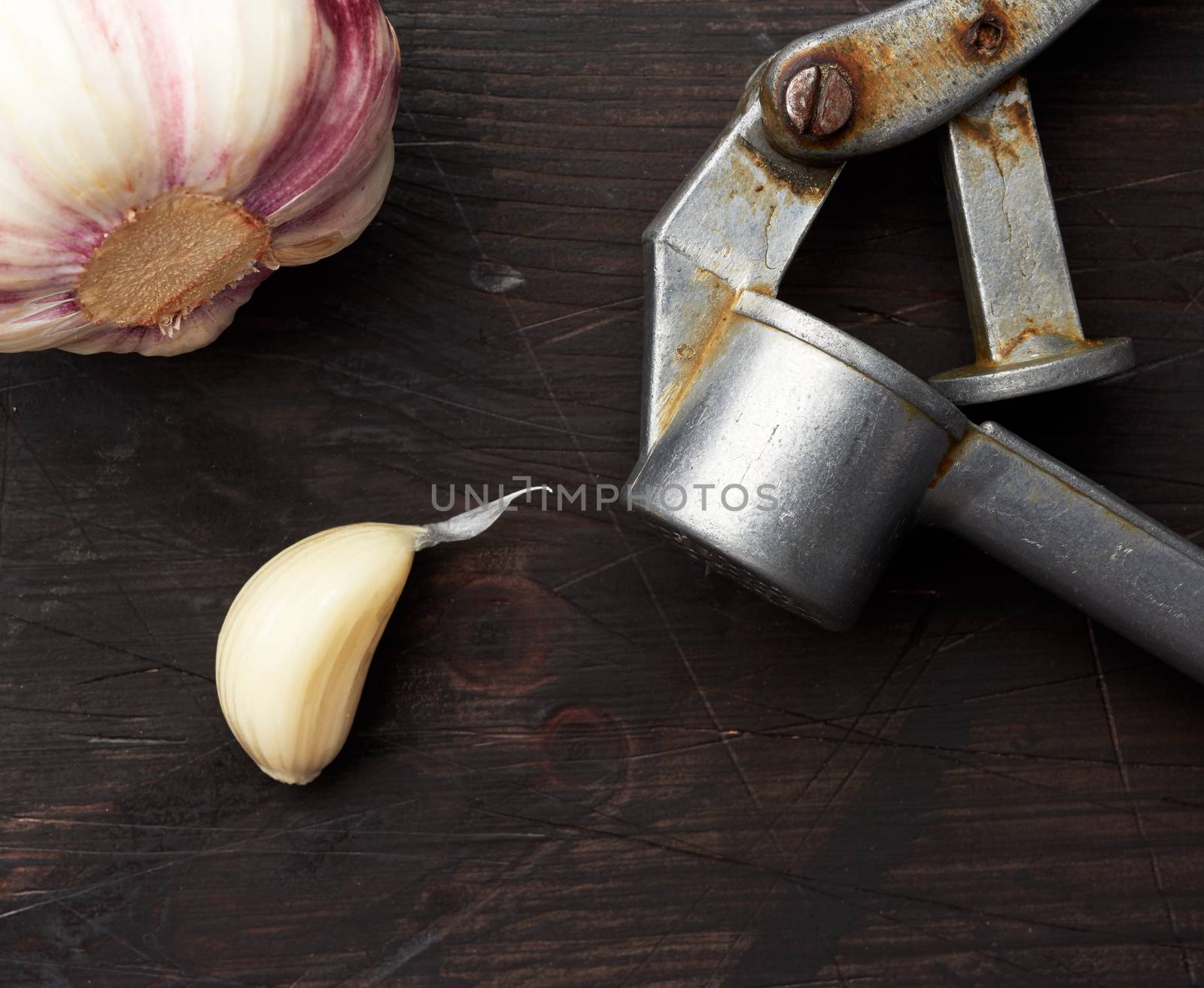 old metal garlic press and fresh young white garlic on a brown wooden table, top view