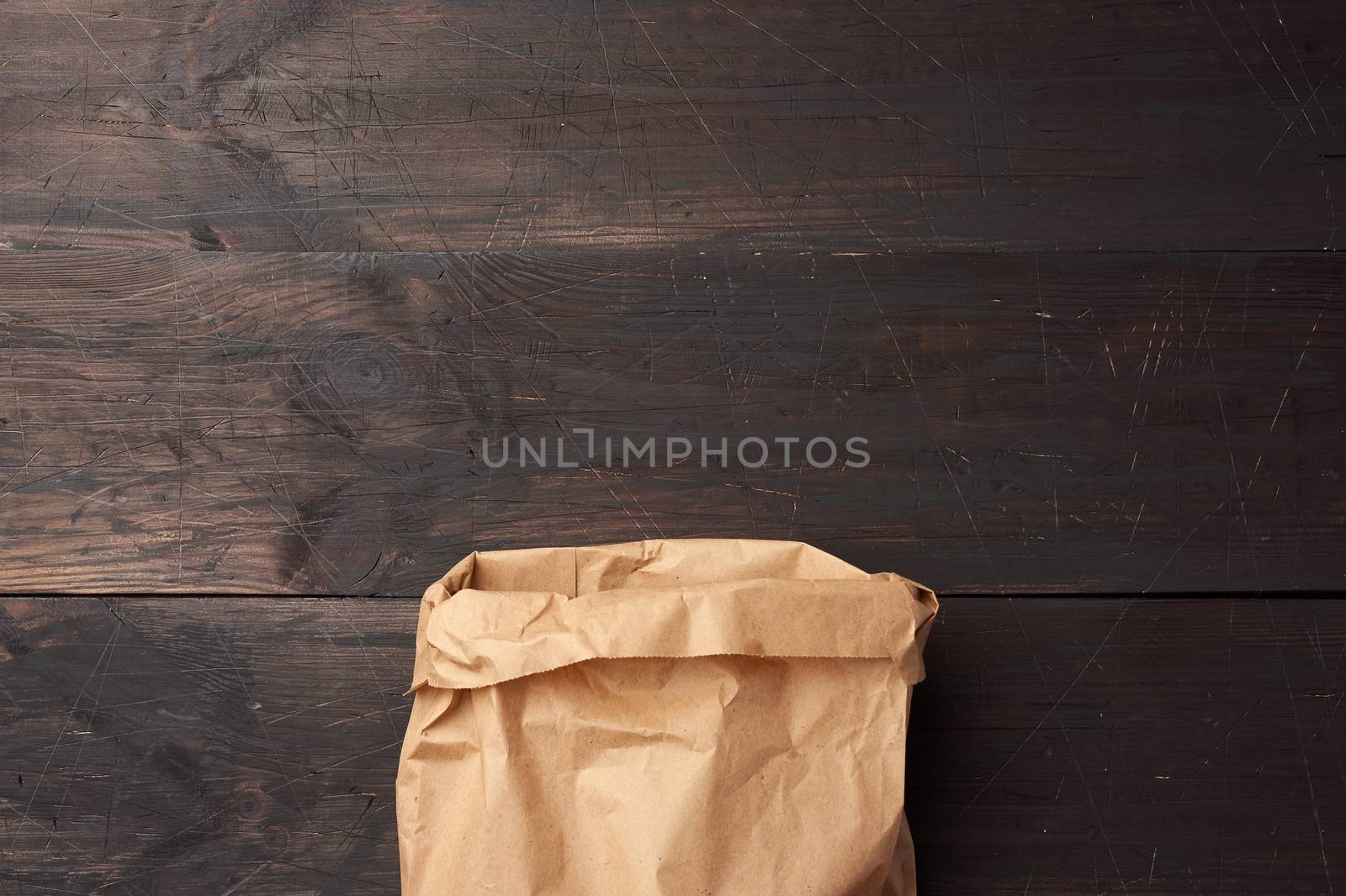 open brown paper bag for food packaging on a brown wooden background, concept of rejection of plastic bags to save the environment