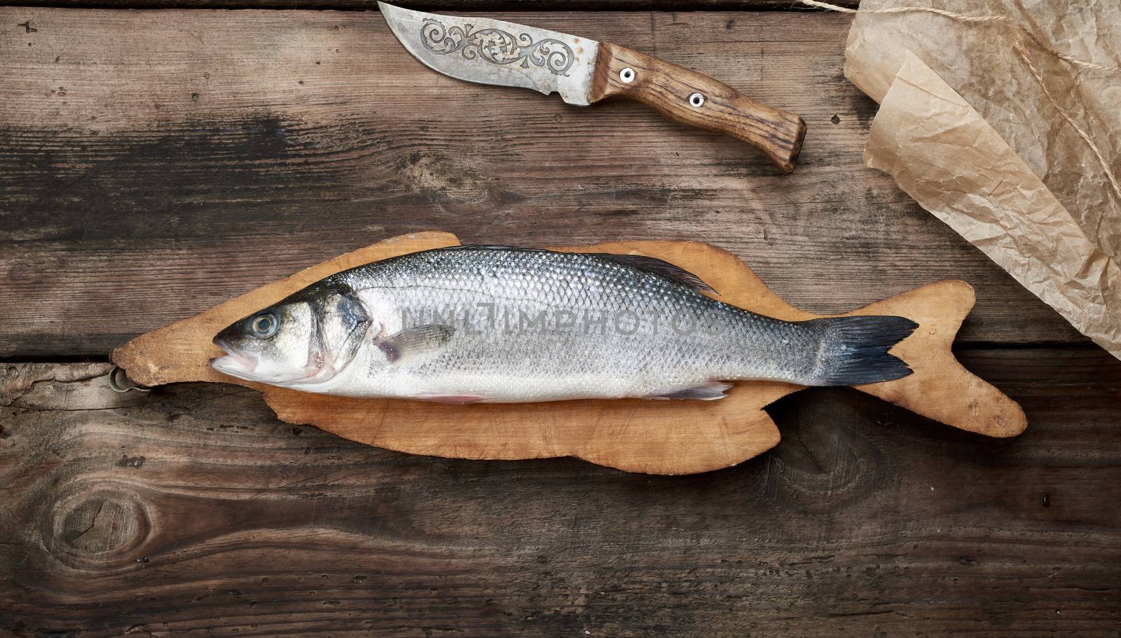 fresh whole sea bass fish on brown cutting board, top view