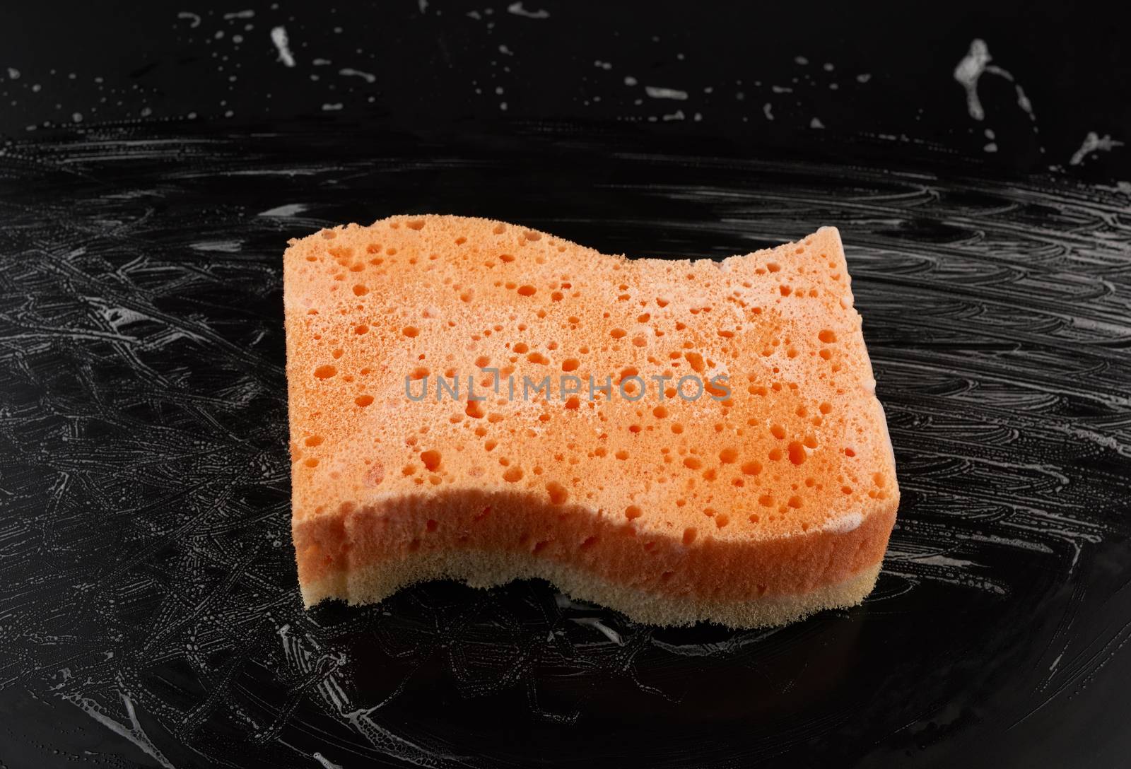 rectangular wet orange washcloth with white foam on a black background, top view