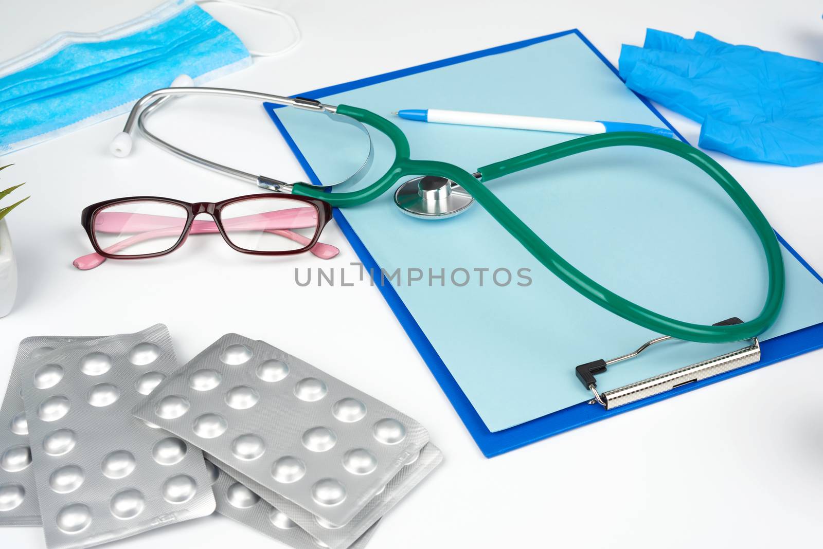 metal stethoscope, paper holder with a blank blue sheet, disposable blue medical mask on a white background, top view