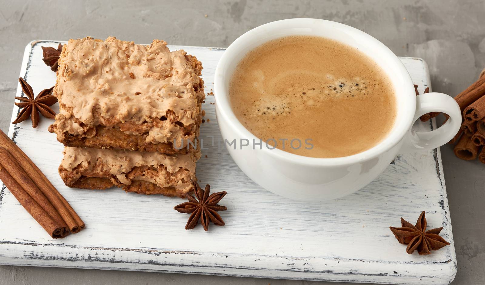 stack of baked Krakow meringue cookies on a wooden board and a white ceramic cup with black coffee, delicious dessert of whipped egg whites and almond flour