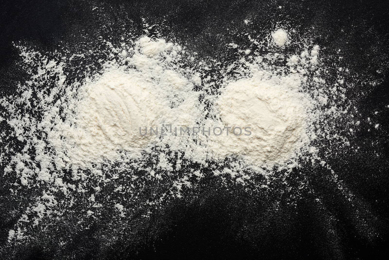 white wheat flour scattered on a black table, ingredient for the dough, top view