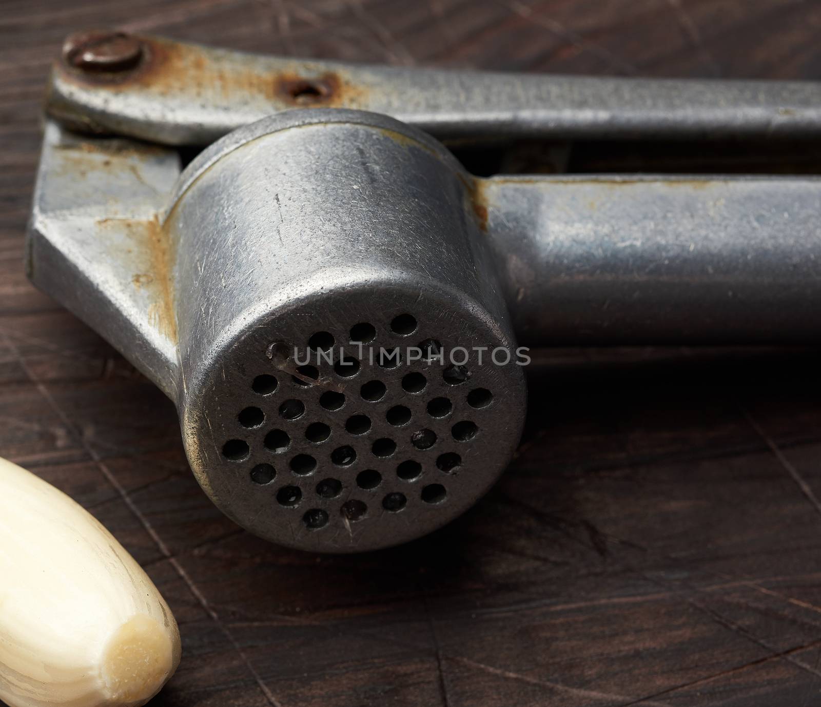 old metal garlic press and fresh young white garlic on a brown wooden table, close up