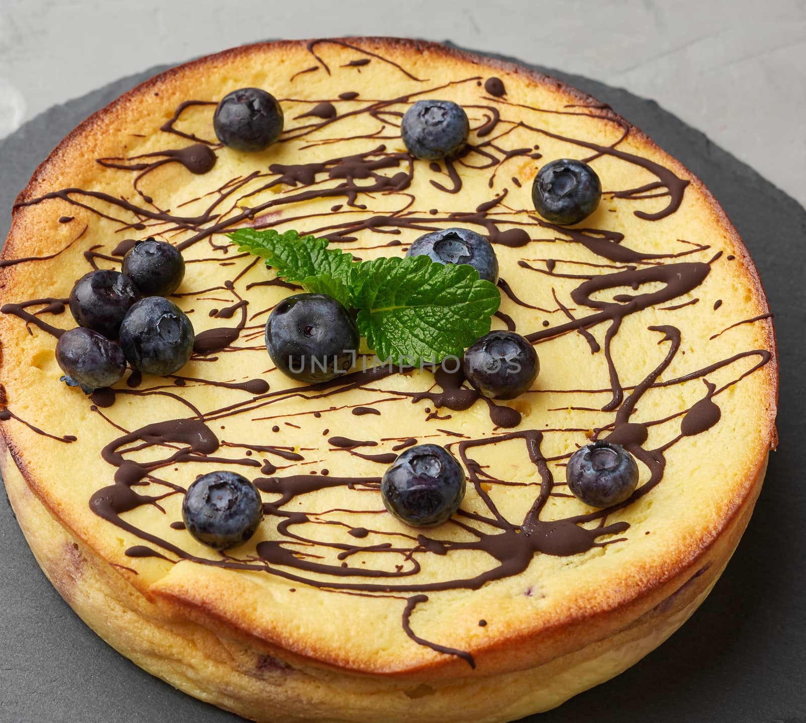 baked round cottage cheese casserole on a black plate, top view, tasty and healthy dessert