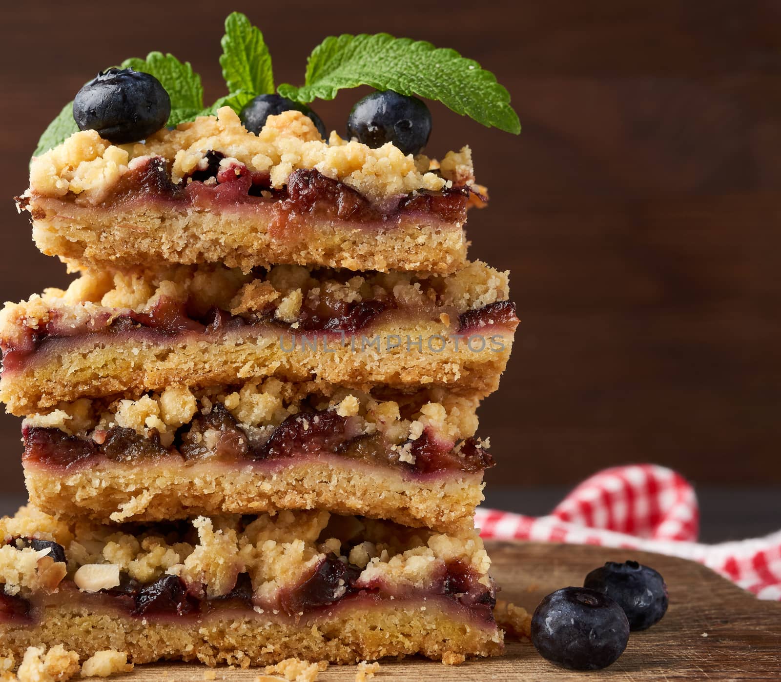stack of square slices of baked crumble pie with blue plum on a wooden board, delicious dessert