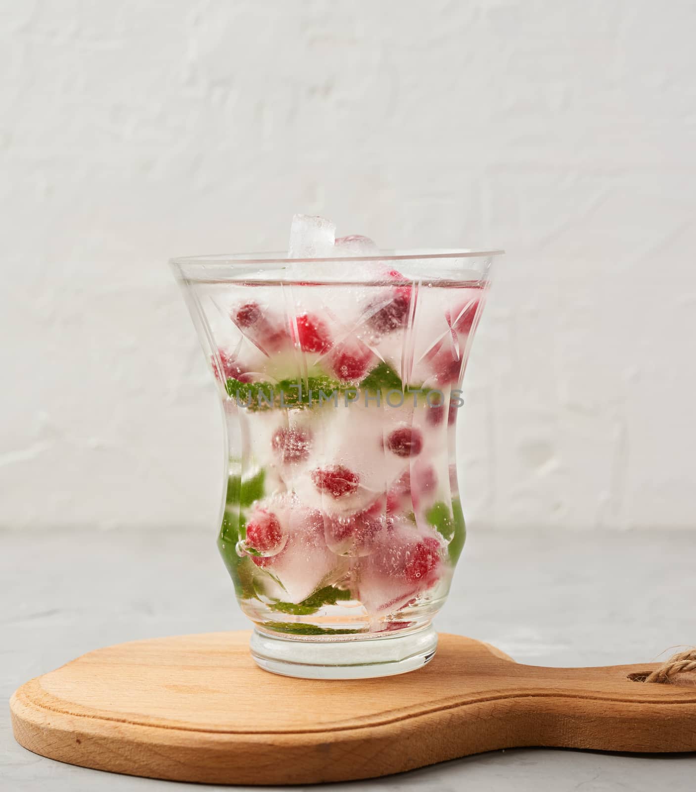 transparent glass with lemonade and pieces of ice, red berries on a white background, a refreshing summer drink