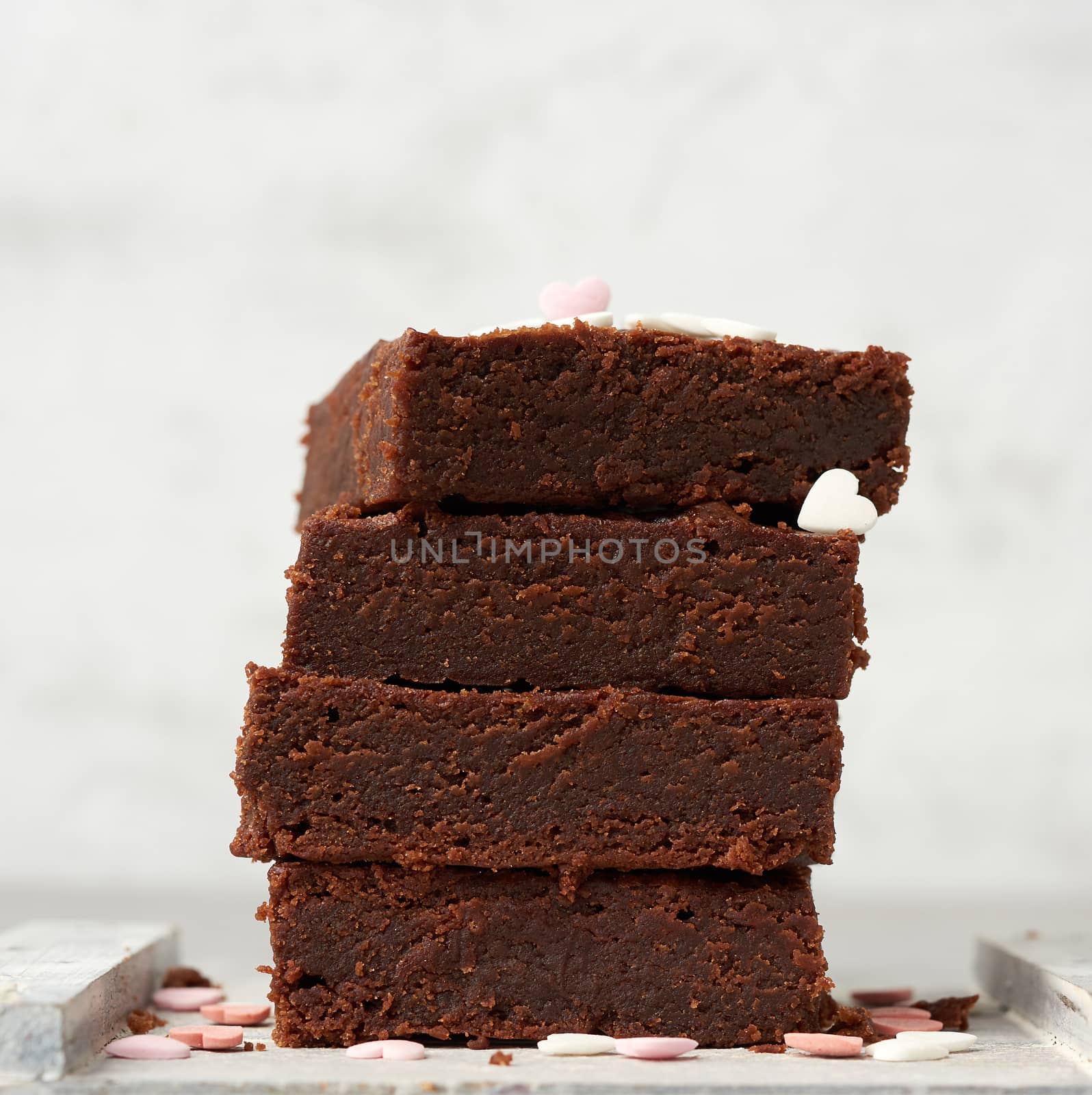 stack of square baked brownie chocolate cake slices on a white background, delicious dessert, close up