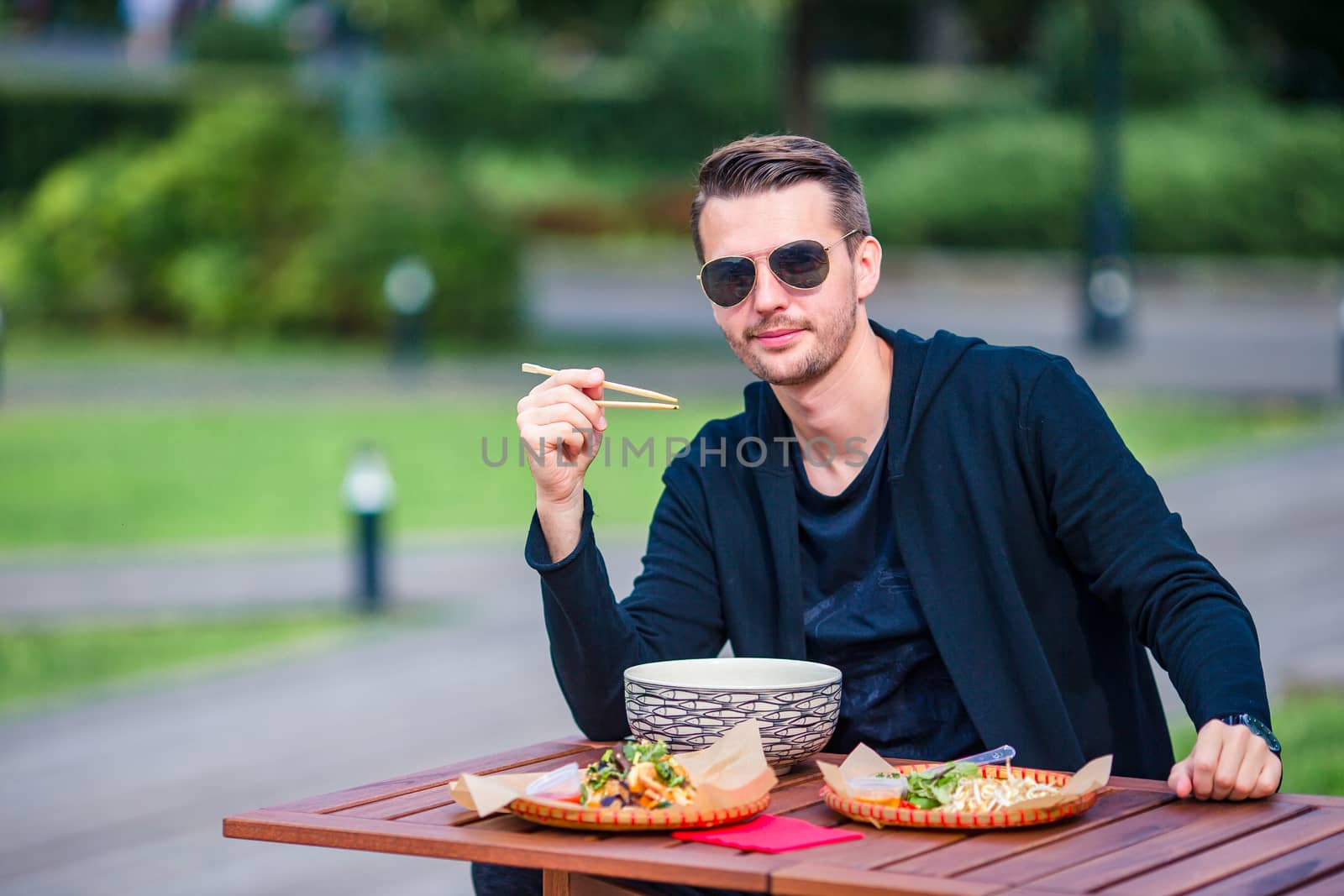 Young man eating take away noodles on the street by travnikovstudio