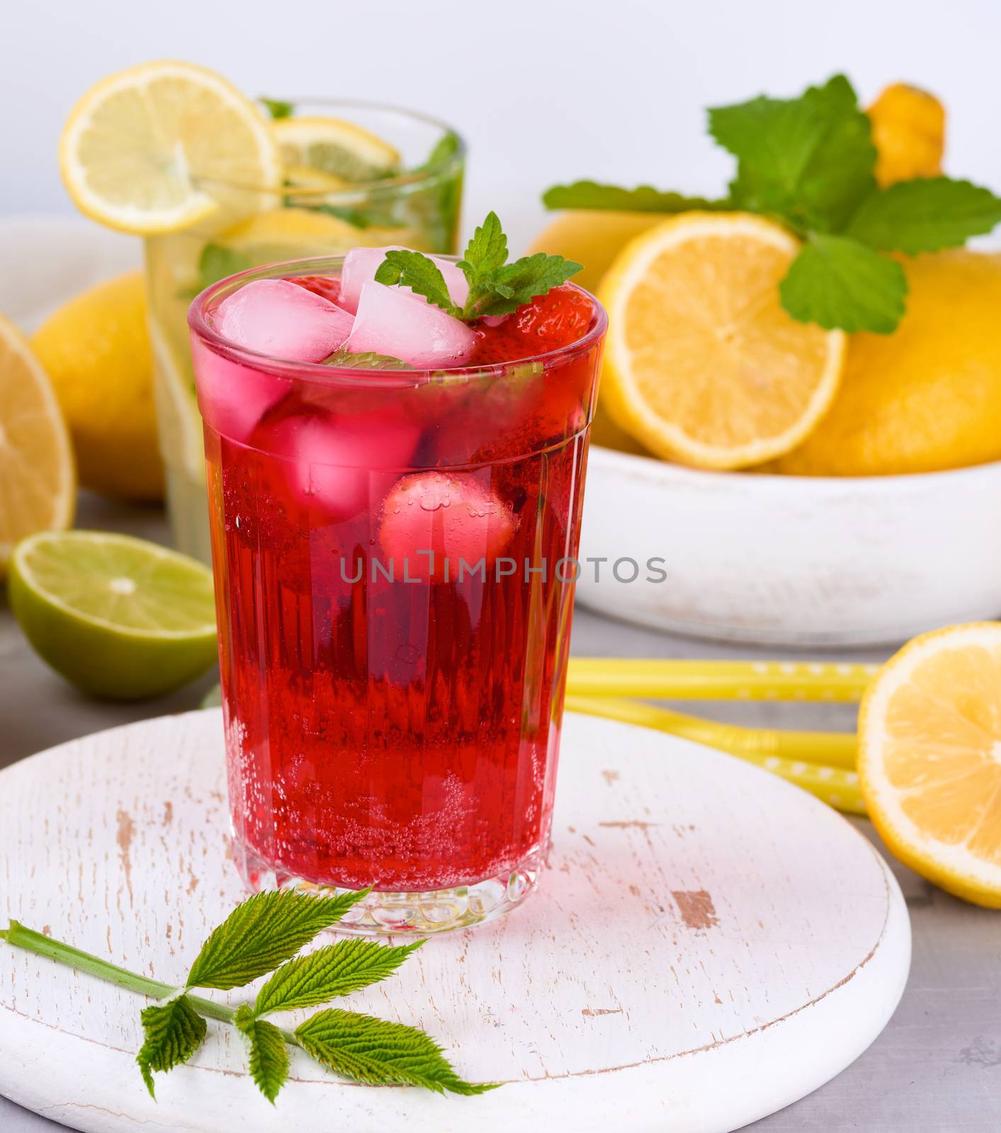 refreshing summer drink of strawberries and cranberries on a white wooden board, behind it are yellow lemons and green mint leaves