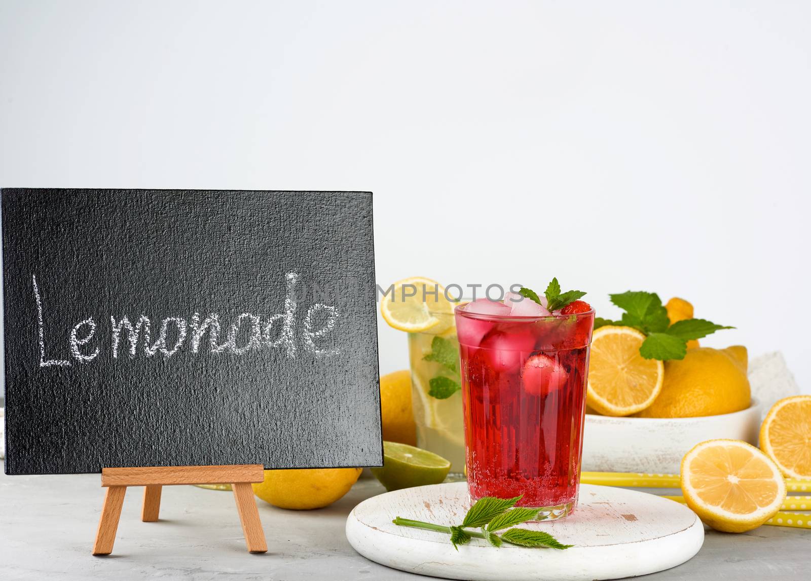 black chalk board for writing a summer drink recipe and a glass with berry lemonade, fresh yellow lemons and mint green behind