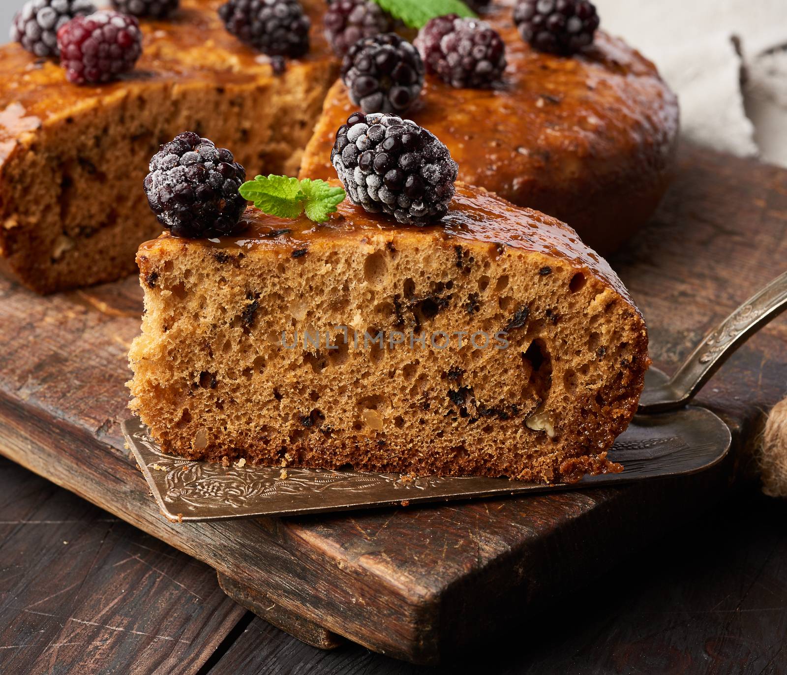 baked round sponge cake with nuts and topped with berries, wooden brown table, close up