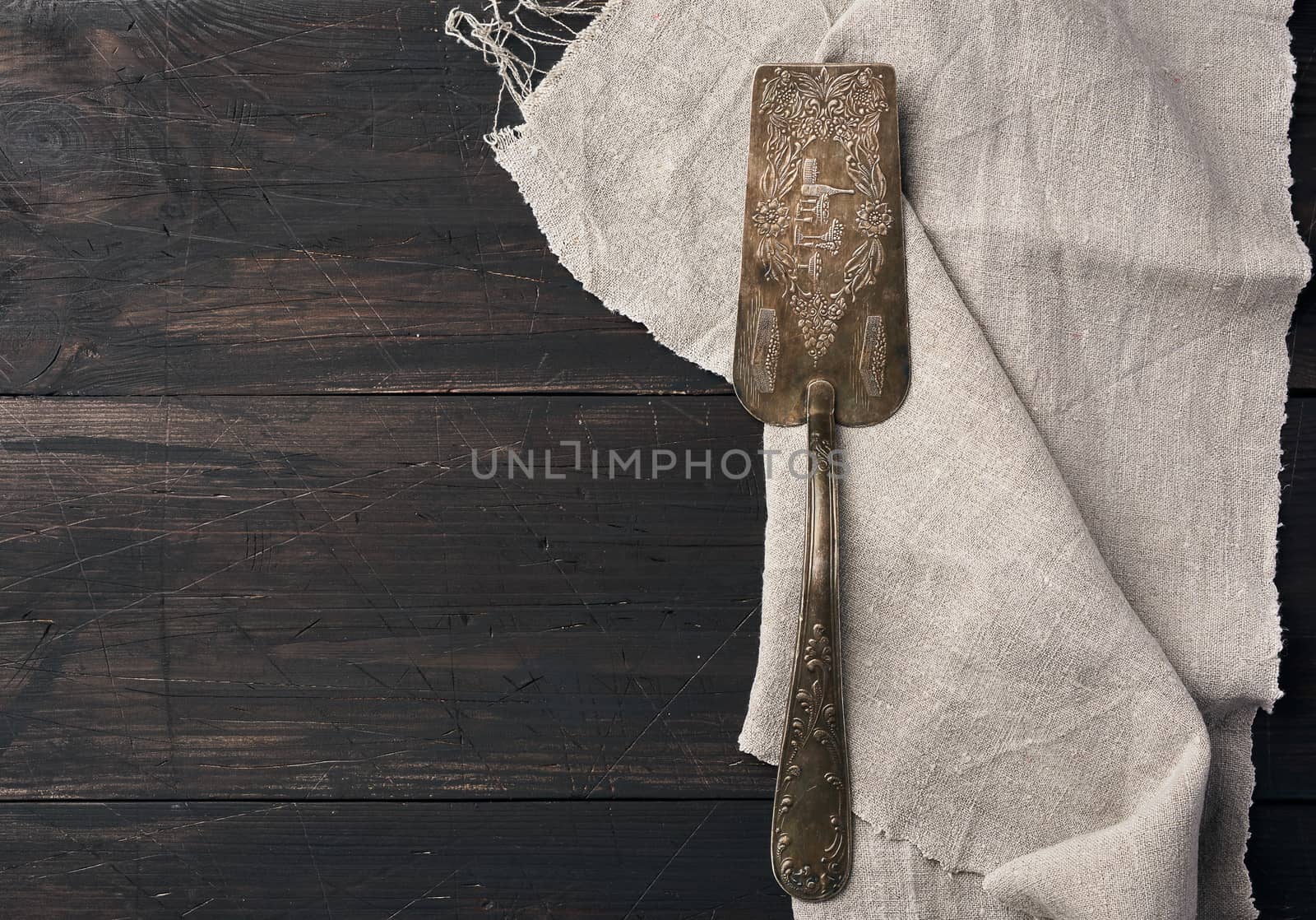 metal spatula for cakes on a brown wooden background with a gray linen towel, top view, place for an inscription