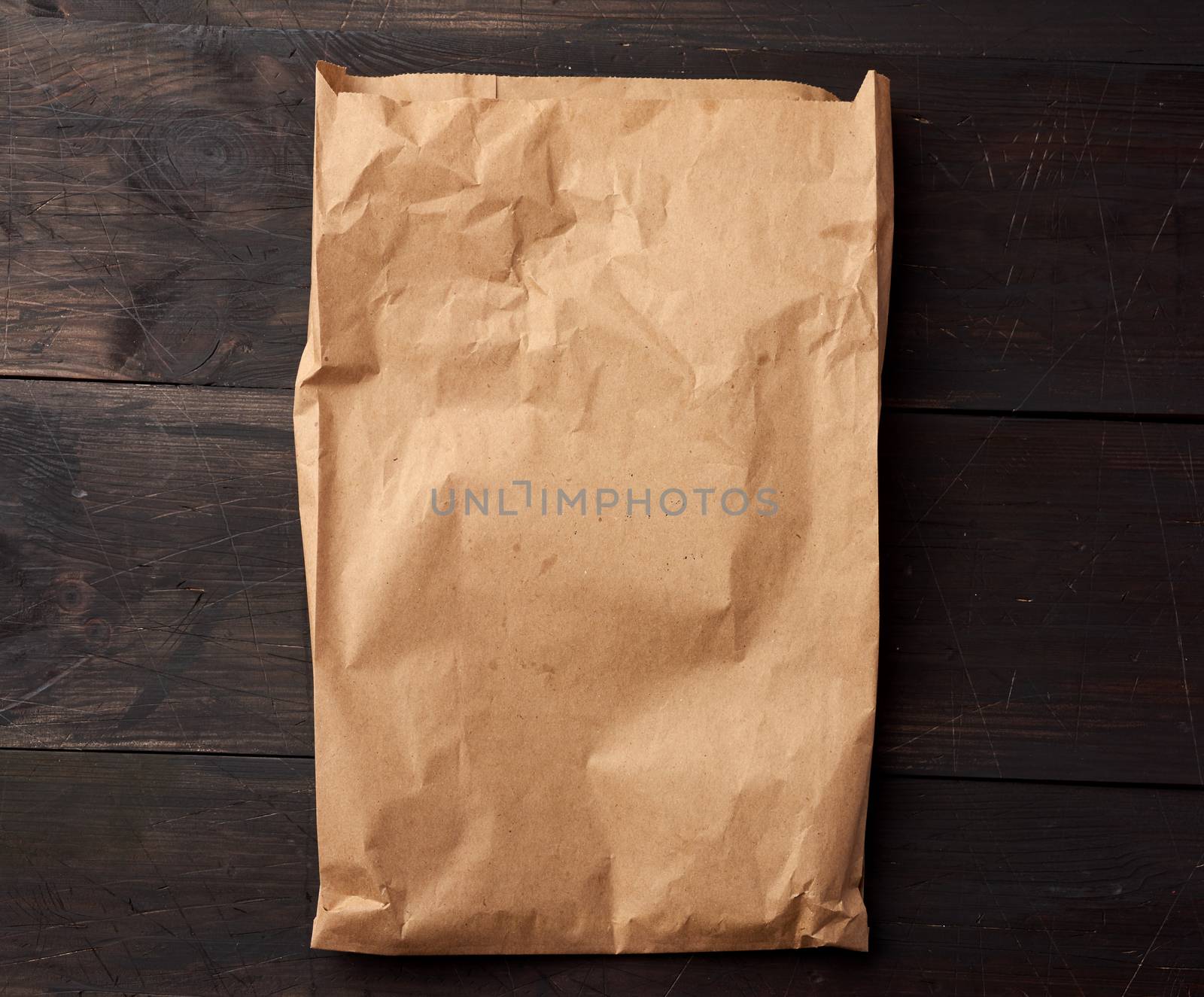 open brown paper bag for food packaging on a brown wooden background, concept of rejection of plastic bags to save the environment