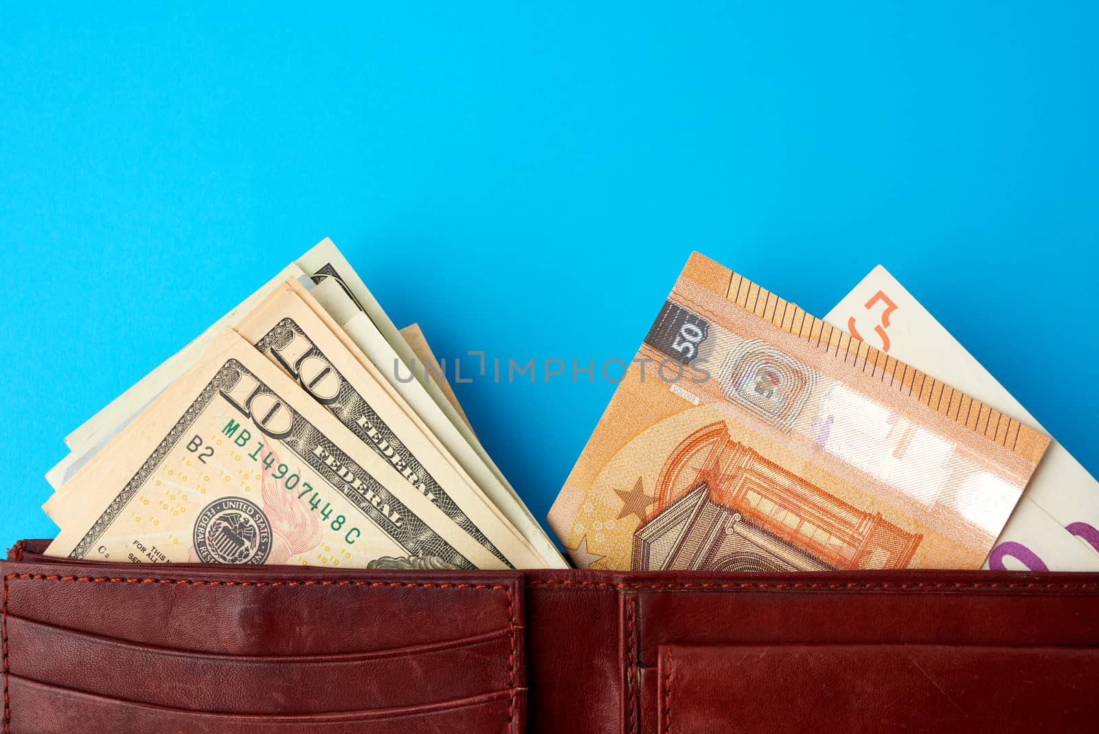 European Union paper money Euro and US dollars in a brown leather wallet on a blue background, concept of wealth, exchange investment, crisis