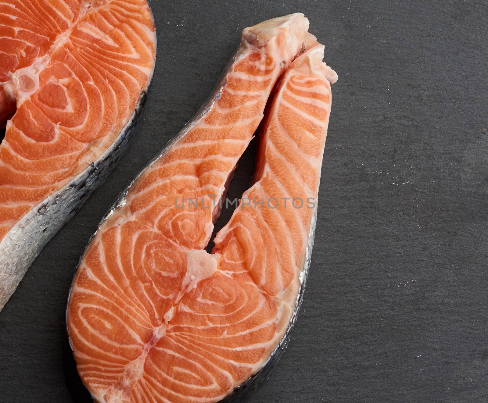 two raw salmon steaks on a black background, top view