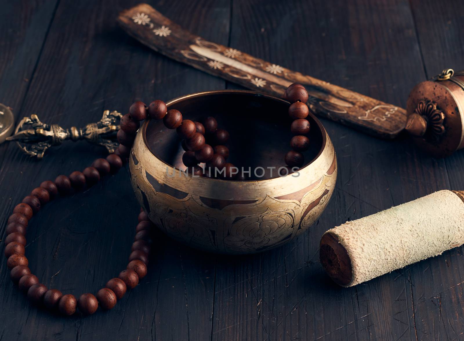 Tibetan singing copper bowl with a wooden clapper on a brown wooden table, objects for meditation and alternative medicine, close up