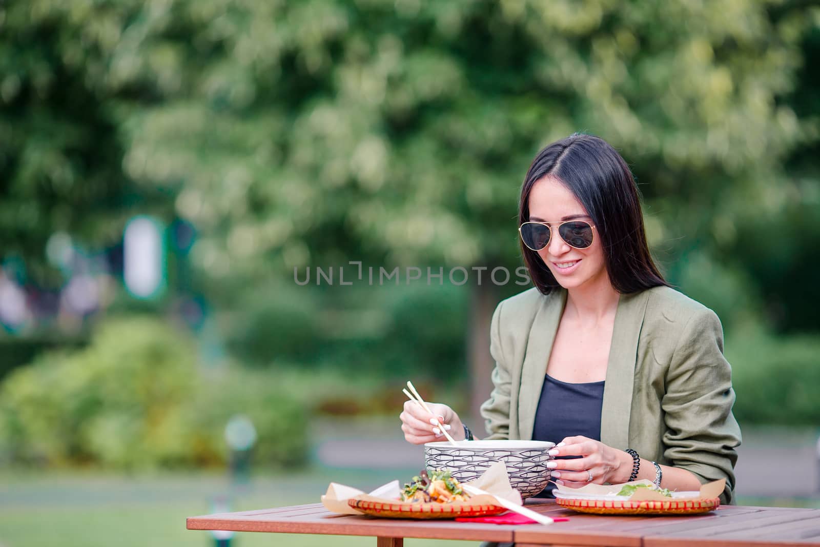 Young woman eating take away noodles on the street by travnikovstudio