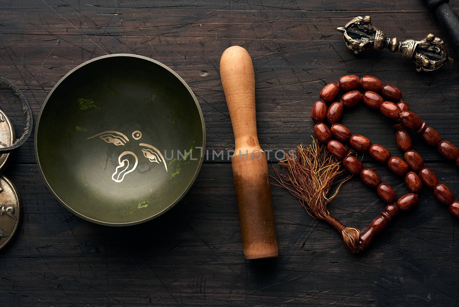 Tibetan singing copper bowl with a wooden clapper on a brown wooden table, objects for meditation and alternative medicine, top view