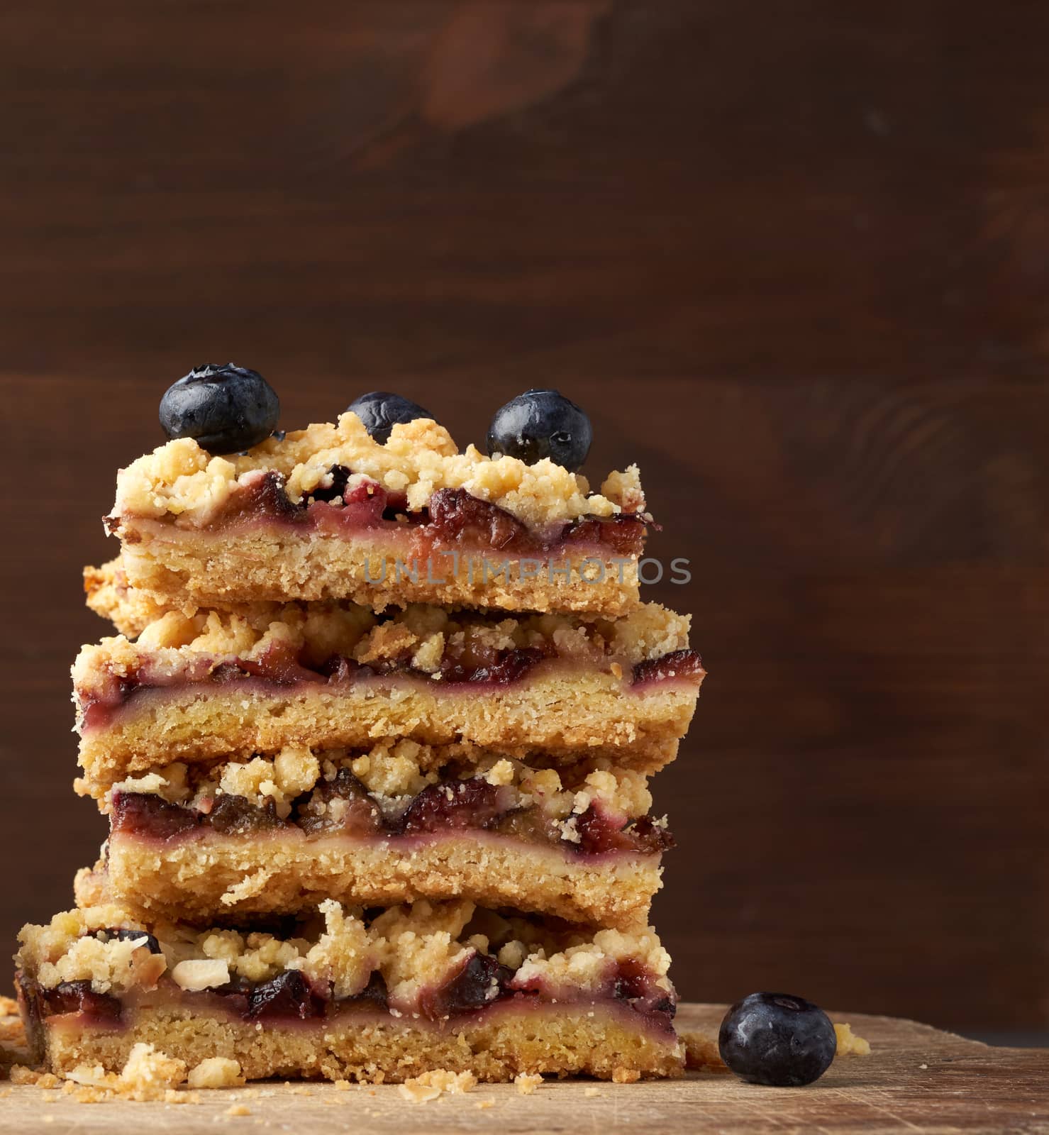 quare slices of baked crumble pie with blue plum on a wooden board, delicious dessert, close up