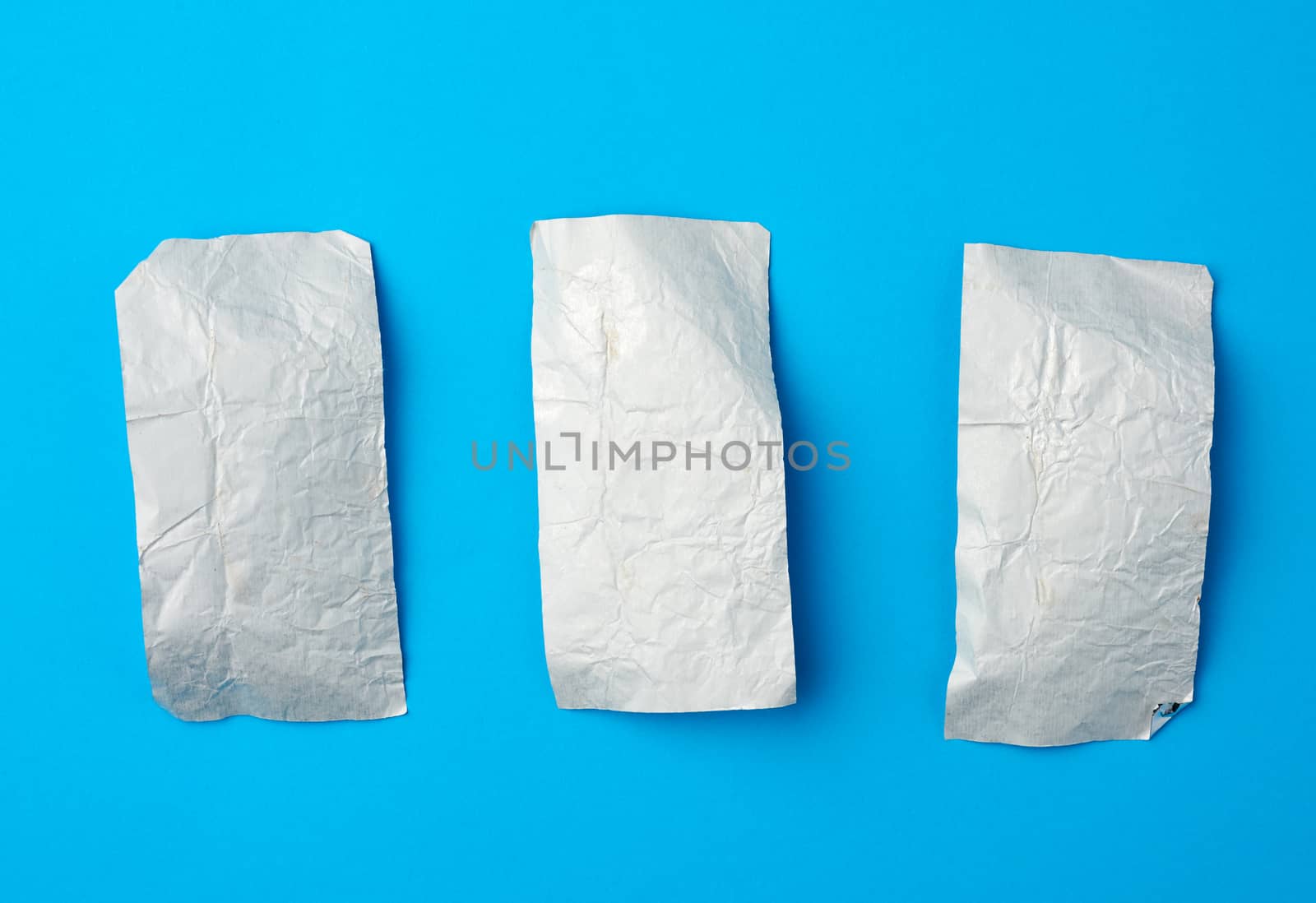various crumpled foil used candy wrappers on a blue background, top view