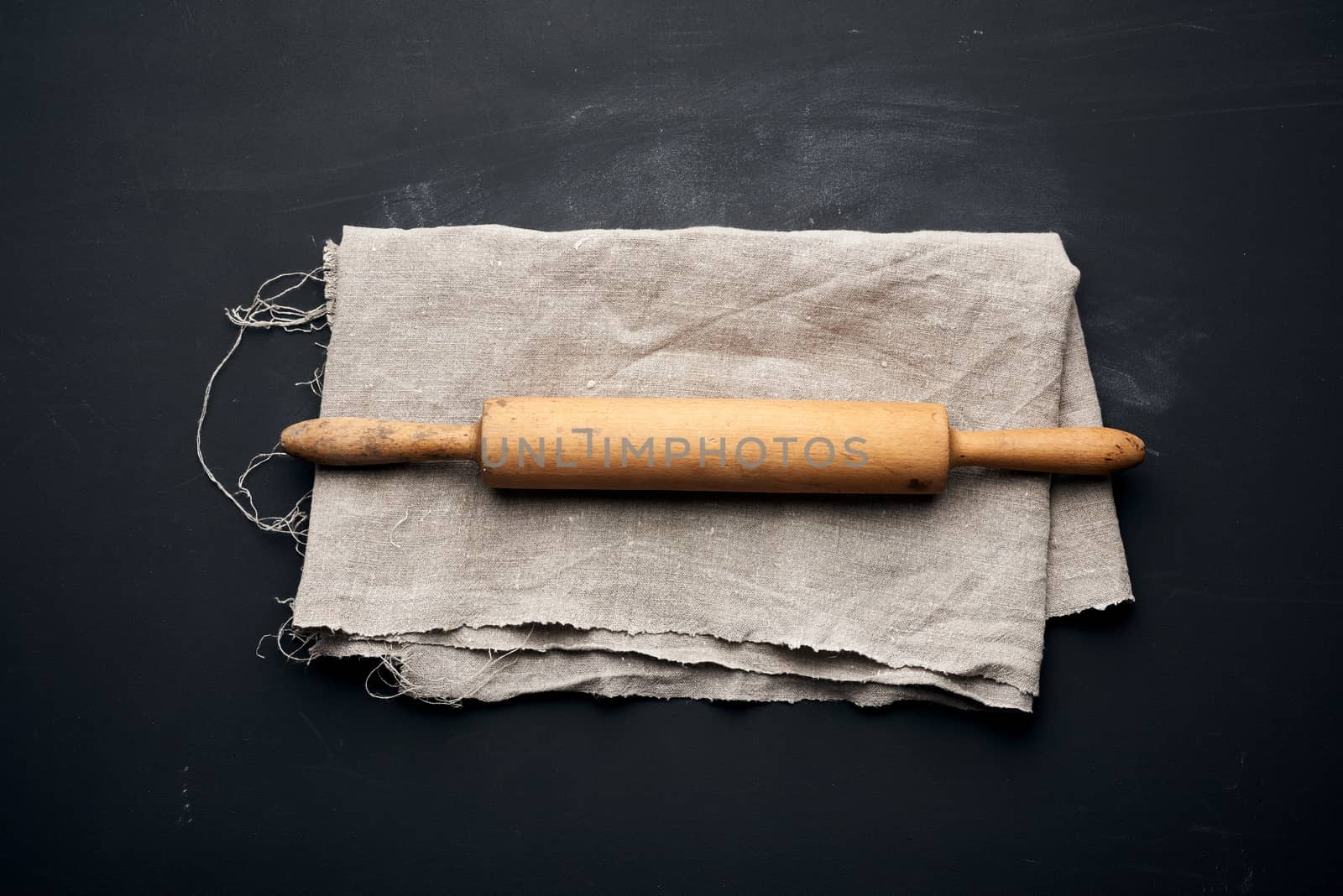 wooden rolling pin lie on a gray linen napkin, black table, top view, copy space