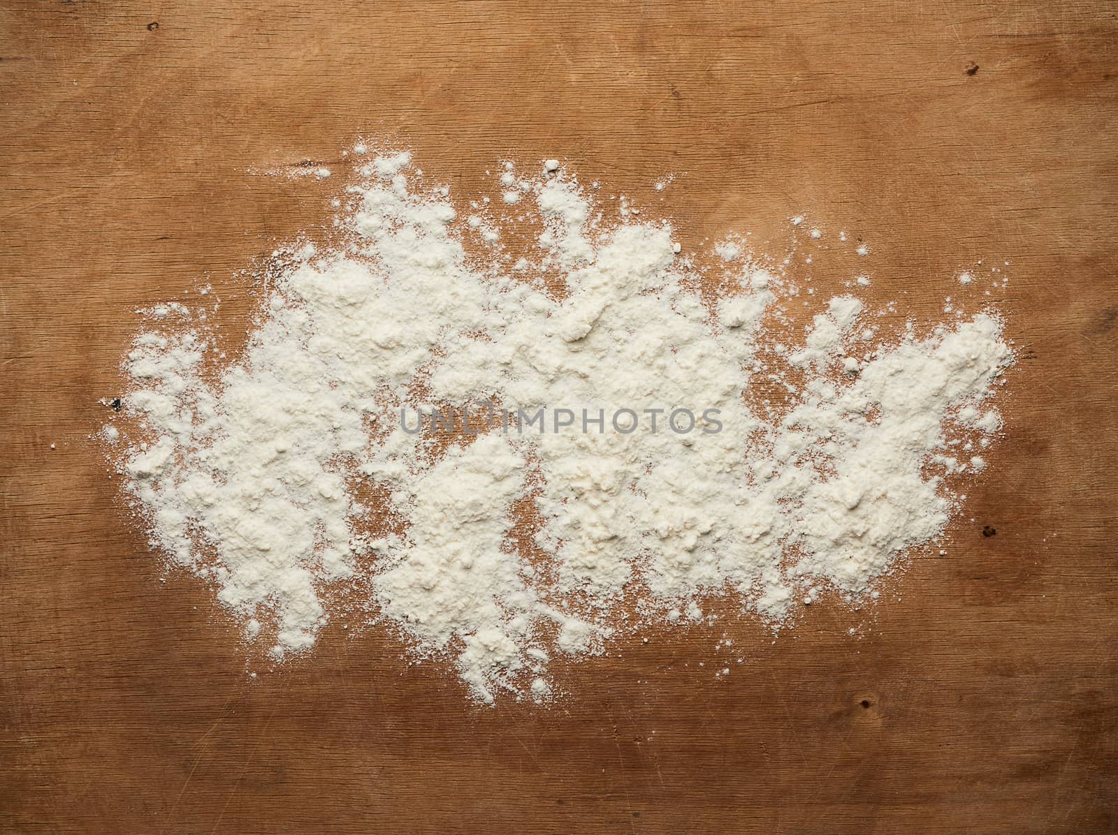 white wheat flour scattered on a brown wooden table, top view, kitchen backdrop