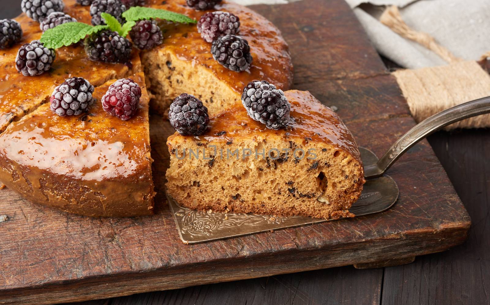 baked round sponge cake with nuts and topped with berries, wooden brown table, close up
