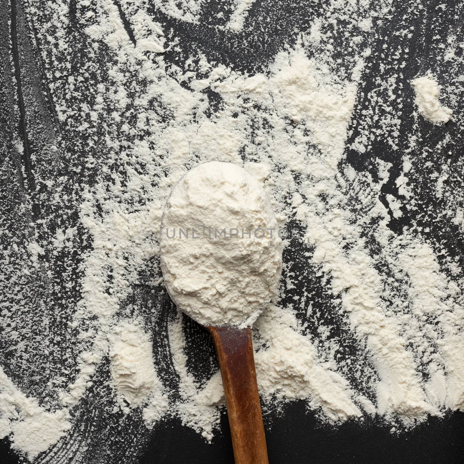 white wheat flour in a wooden brown spoon, black background, close up