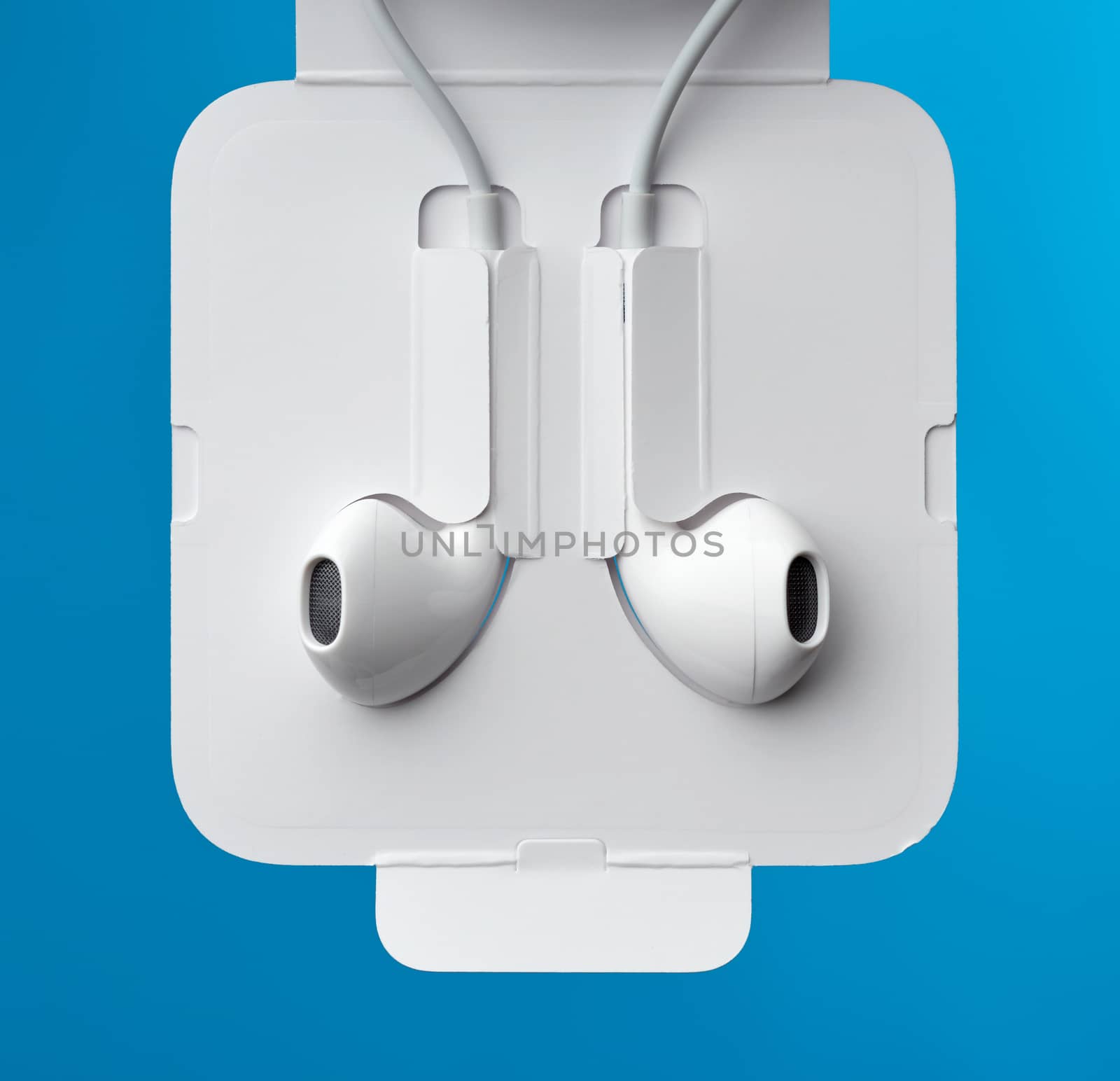 hanging headphones on a white cable, a modern gadget on a blue background, close up, product is packed in carton